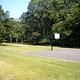 Left side of a basketball court showing a hoop, with trees in the background.  