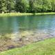 Pond shoreline view with clear water and surrounding trees and turf — shows on-site water feature/landscape amenity (appears on the site’s main pages).