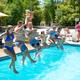 Multiple people jumping into the outdoor pool with park mascot statue visible in background — clear photo of the resort pool amenity from the gallery/slider. 