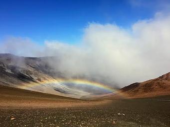 view of crater, orange and black cinder hills with clouds and a low rainbow 