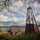 View of a wood cabin and windmill in a grassy field with a lake and mountains in the background.