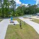 RV park with concrete pads, picnic tables, and RVs parked, surrounded by trees.