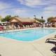 Alternate pool-facing shot with lounge chairs and clubhouse visible — clear depiction of the resort’s swimming amenity and seating areas from the homepage imagery.