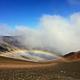 view of crater, orange and black cinder hills with clouds and a low rainbow 