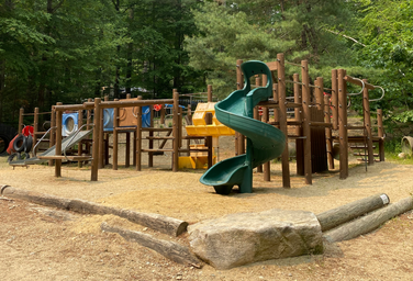 Outdoor playground structure (slides, climbing elements) on wood-chip surface — clear image of on-site family amenities referenced on the property website.