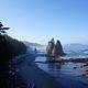 Rocky sea stacks rise from the sandy, ocean shore just south of Hole-in-the-Wall. Driftwood lays scattered on the beach.