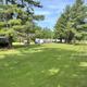 Daytime view of multiple RV sites and a gravel access road across a mowed field with shade trees — matches the 'Site Information' page and shows the campground layout and pitches.