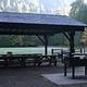 Group picnic shelter and barbecue next to large flat lawn ringed by mostly conifer forest.