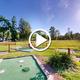 Wide view of campground grounds and on-site mini-golf (video thumbnail) showing open lawn, walkways and RVs in background — useful aerial/overview of the property as presented on the home page video.