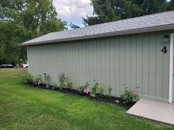 Side view of a numbered cabin building ("4") with lawn and planted border — shows cabin exterior detail and campsite landscaping from the property photo set.