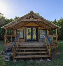 Front view of a larger wooden cabin with porch and steps — shows another lodging/facility type and outdoor seating area promoted on the site.