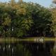 Wide lakeshore view across the water showing treeline, shoreline with small dock and camping area — good overall property overview. Sourced from the Our Campground page (EPLC-23) representing the campground’s lake frontage.