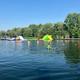 Another broad lake panorama with swimmers and the inflatable course visible, offering a clear daytime view of the lake, beach area and surrounding tree-lined grounds (from the Lake Park page).