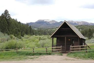  Brown forest service cabin surrounded by green trees and rolling hills
