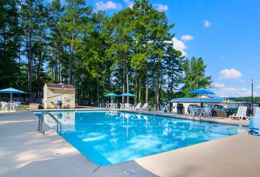 Clear daytime photo of the pool area with chairs, umbrellas and trees — shows an on-site recreational facility. Shown on the resort’s photo gallery page (page: Lake Gaston RV Camping | Thousand Trails RV Campground, URL provided).