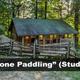 Rustic studio cabin ('Gone Paddling') photographed from the front with steps, porch and wooded terrain — another distinct on-site cabin view from the homepage.