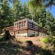 Trail leading to white cabin with wrap around porch, surrounded by fir trees