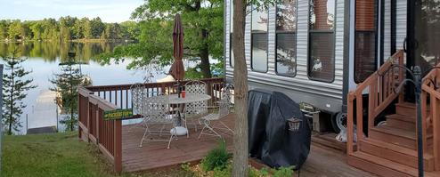 Deck area next to an RV with a view down to the dock — demonstrates RV site patio setup and proximity to the lake and private dock (from the homepage gallery).