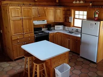 View of the kitchen in the Hillside Cabin with wood cabinents refrig, stove, and island bar with 2 stools
