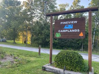 Photograph of the carved wooden entrance sign reading 'PINEVIEW CAMPLANDS' at the roadside — good identification image used on the site's Book Tour / contact areas to mark the property entrance.