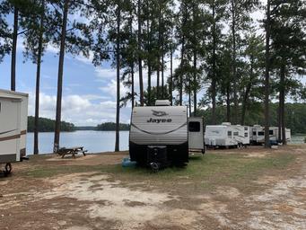 Row of RVs/campsites along the shoreline with picnic table and water visible—shows campsite/RV pitch area (Split Oaks campground section).