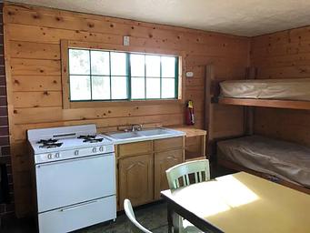 Cabin interior showing gas range, bunkbeds, table and dry sink 