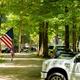 Driveway/road through wooded RV sites showing vehicles and flags — illustrates the seasonal/long-term camping area and campsite layout. From the Seasonal Camping page.