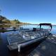 Pontoon boat docked on a wooden pier next to a lake under a clear, blue sky.