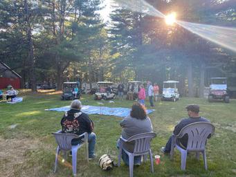 Evening gathering on a lawn with chairs, golf carts and pine trees — conveys community events and the wooded setting of the campground; sourced from the site's Activities page.