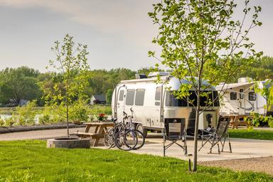 Close view of RV slip/parking pad with picnic table, fire ring and lake in background — clear depiction of RV campsites and site amenities.