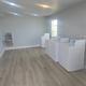 Bright laundry room interior with white coin-operated top-load washers and dryers, wood-look flooring, and a