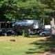 RV and vehicle at a shaded campsite with awning and picnic setup—clear depiction of RV pitches and site layout from the Facilities/The Park page.