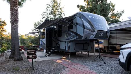 Close view of a large fifth-wheel at a designated long-term/drive-up site, including small signage and site features — demonstrates site size and surfacing.
