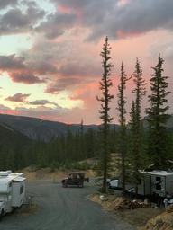 On-site campsite shot at sunset showing RVs, an off-road vehicle and the campground road with surrounding forested mountains — useful for campsite ambience and setting.