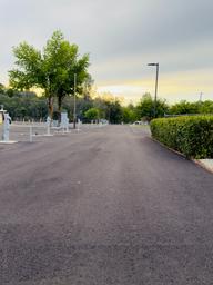 Perspective down a paved driveway/road through the RV park showing hookup stations along the left and hedged perimeter on the right — good orientation shot of park circulation.