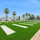 A grassy area with palm trees, evenly spaced white concrete slabs, and RVs in the background under a clear blue sky in apache junction az
