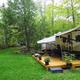 Ground-level view of an RV with a small deck on a grassy wooded site — illustrates seasonal RV campsite accommodations on the property (matches campsite references on the site).
