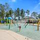 Children's splash pad/shallow pool area with colorful water features and clubhouse in background — highlights family-friendly pool amenities located on the campground grounds.