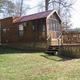 Exterior view of a rustic cabin on a raised deck with steps and surrounding grounds — represents the campground's cabin rental accommodations.