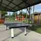 Outdoor covered area with a ping pong table, giant connect four game, and a small wooden shed, with trees and parked cars in the background.