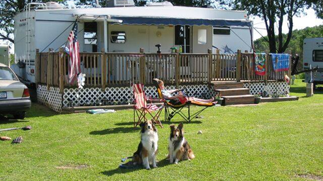 Close-to-mid shot of an RV site with a raised deck, chairs and dogs — shows typical campsite setup and guest amenities (homepage image).
