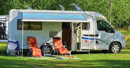 Photo of an RV at a campsite with awning and outdoor chairs; from the site's 'RV' ways-to-stay section — shows typical RV pitch and site setting.