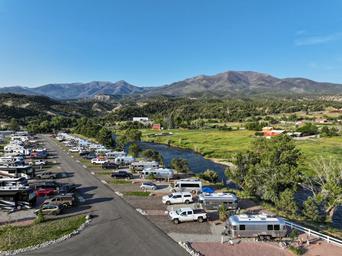 Longitudinal view of RV rows along the river showing individual pads, vehicles and river frontage — demonstrates campsite spacing and river access; used on extended-stay page.