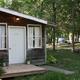 Cabin in a wooded setting with RVs visible in the background — shows lodging/campsite units and site layout from the Campsite page.