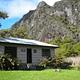 tan cabin with lush greenery surrounding with tall cliff in background