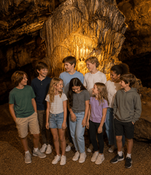 Well-lit interior shot of a large cave formation with a group of children — highlights the cave attraction and guided-tour experience (used on Birthdays page).
