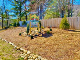 Entrance or property sign on landscaped mound with fencing and trees visible — clear identification of the campground entrance/branding on the gallery page.