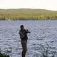 Angler standing at the shoreline with lake and tree-lined opposite shore visible — illustrates fishing access and lakeside scenery (source: Boating page).