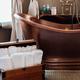 Copper bathtub in luxury bathroom with rolled white towels and accessories.
