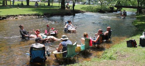 Shows people relaxing in the shallow creek that runs through the property — highlights a distinctive on-site water recreation feature (slider5 image).